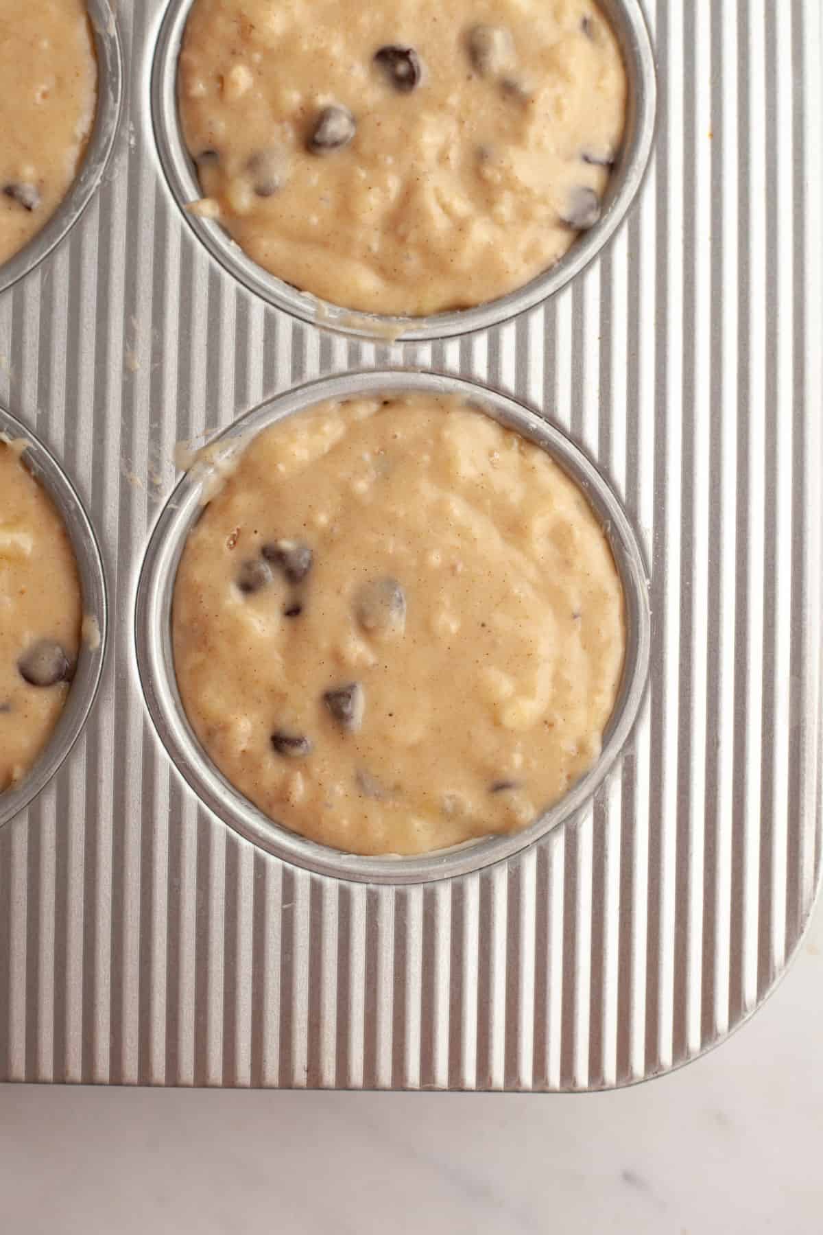 Unbaked chocolate chip banana muffins in a muffin pan.