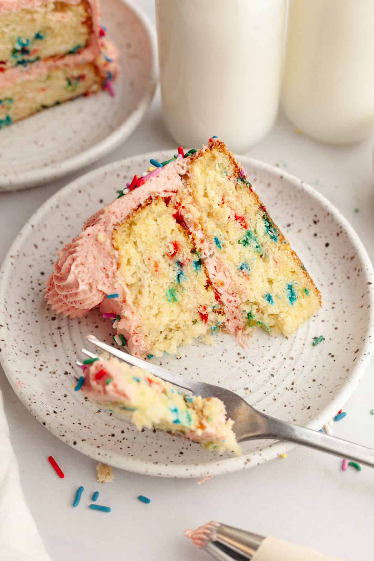 A slice of strawberry funfetti cake on a small plate, a bite has been taken out of it.