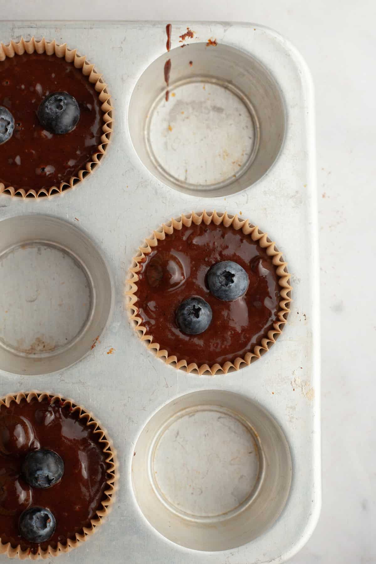 Unbaked chocolate blueberry muffins in a muffin pan.