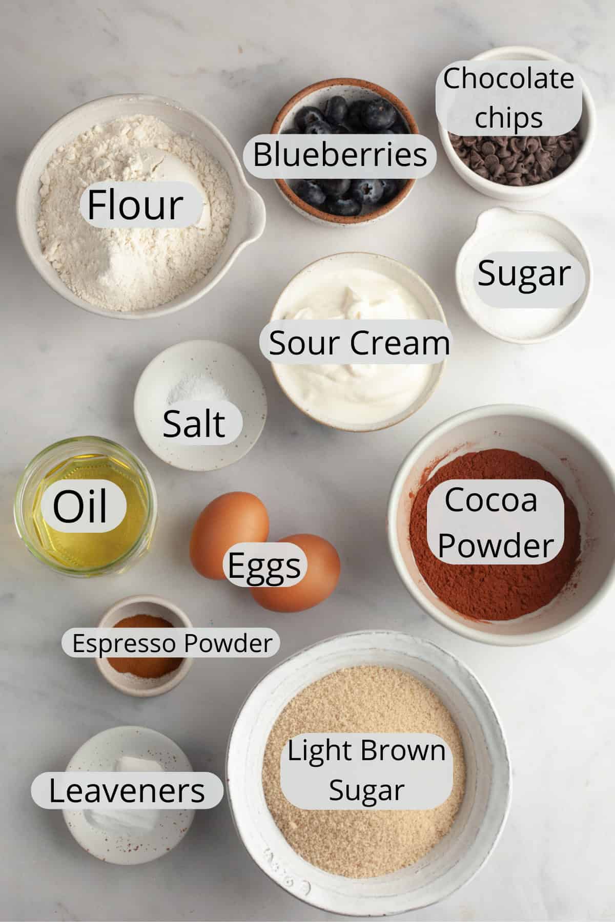 All the ingredients needed to make blueberry chocolate muffins, weighed out into small bowls.