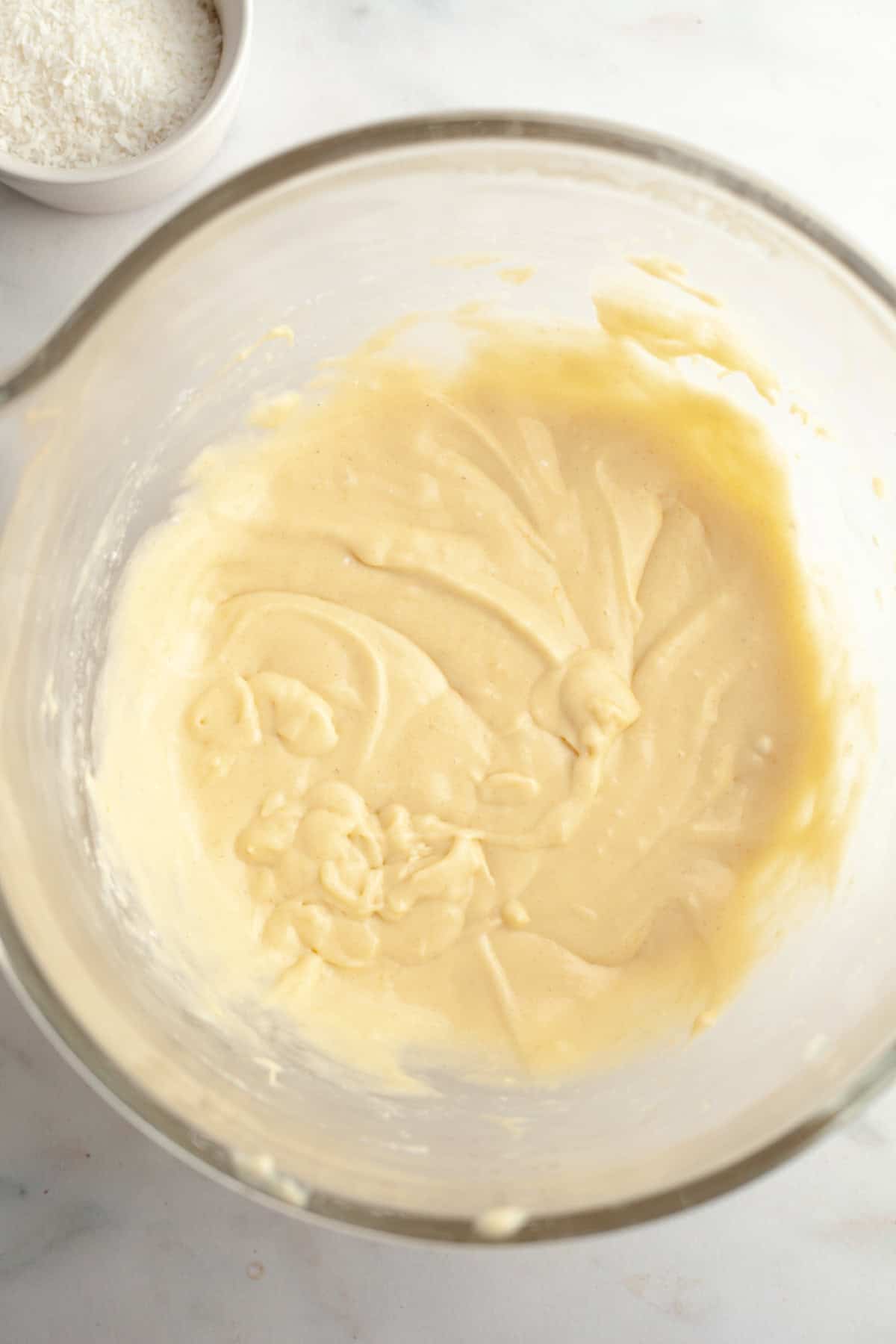 A yellow cupcake batter in a glass mixing bowl.