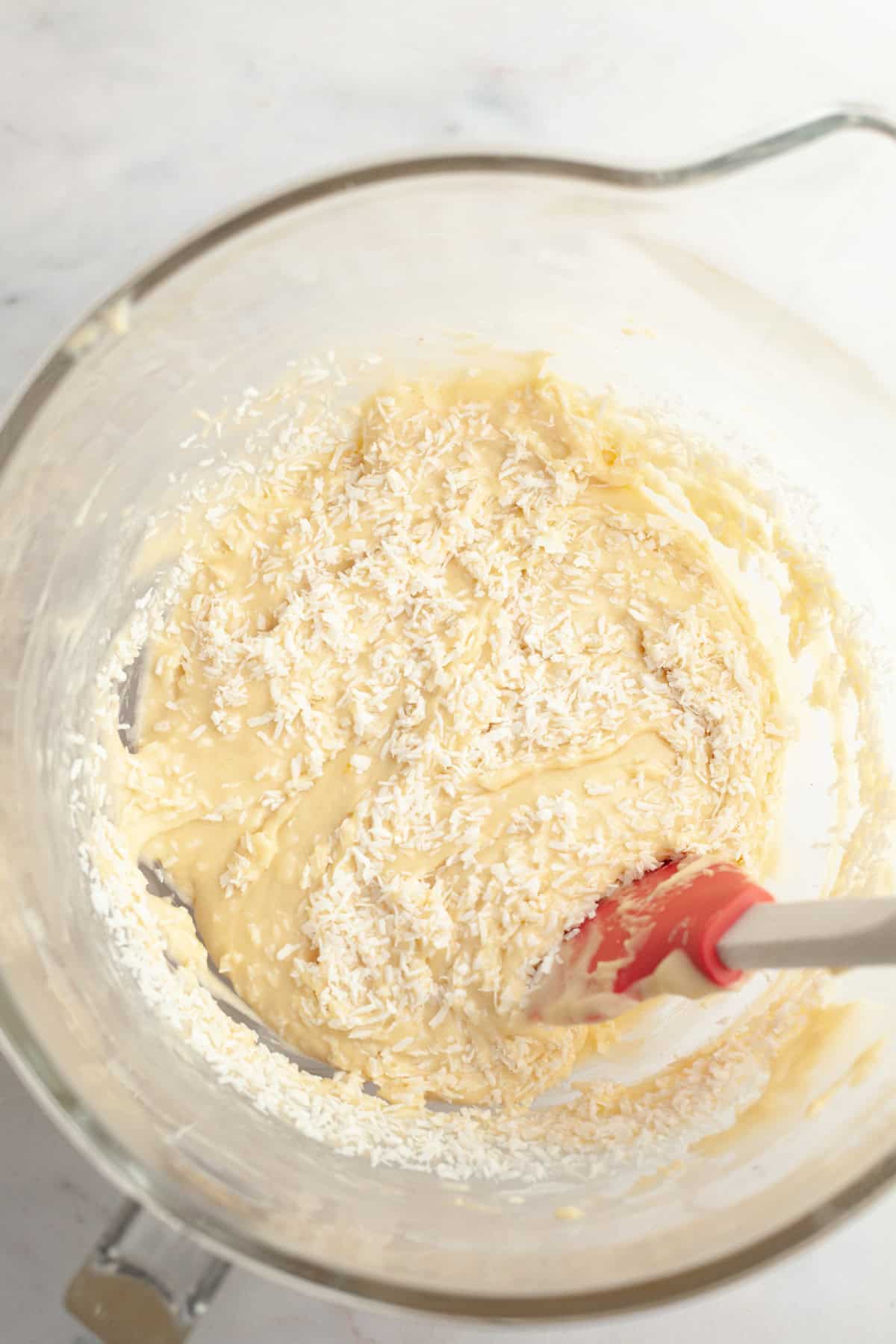 A yellow cupcake batter with shredded coconut in a glass mixing bowl.
