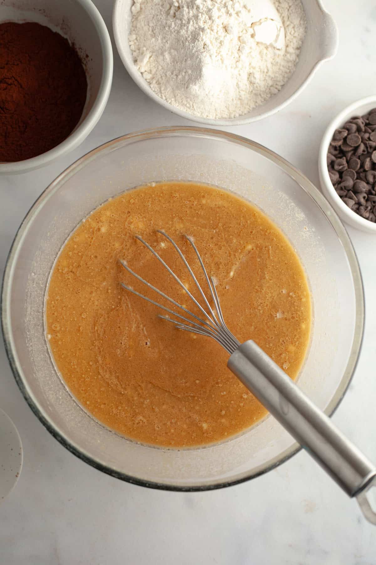 Oil, coffee, eggs, and sour cream mixed together in a glass bowl with a whisk.