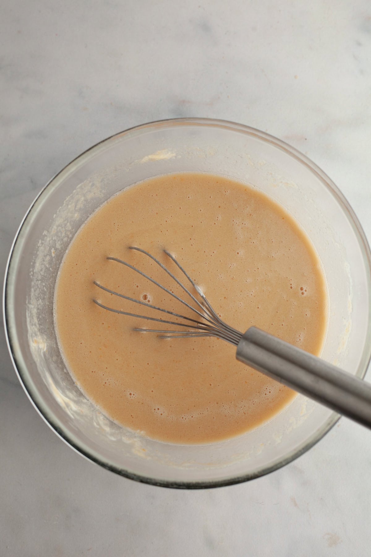 A glass bowl with a beige mixture in it and a whisk.