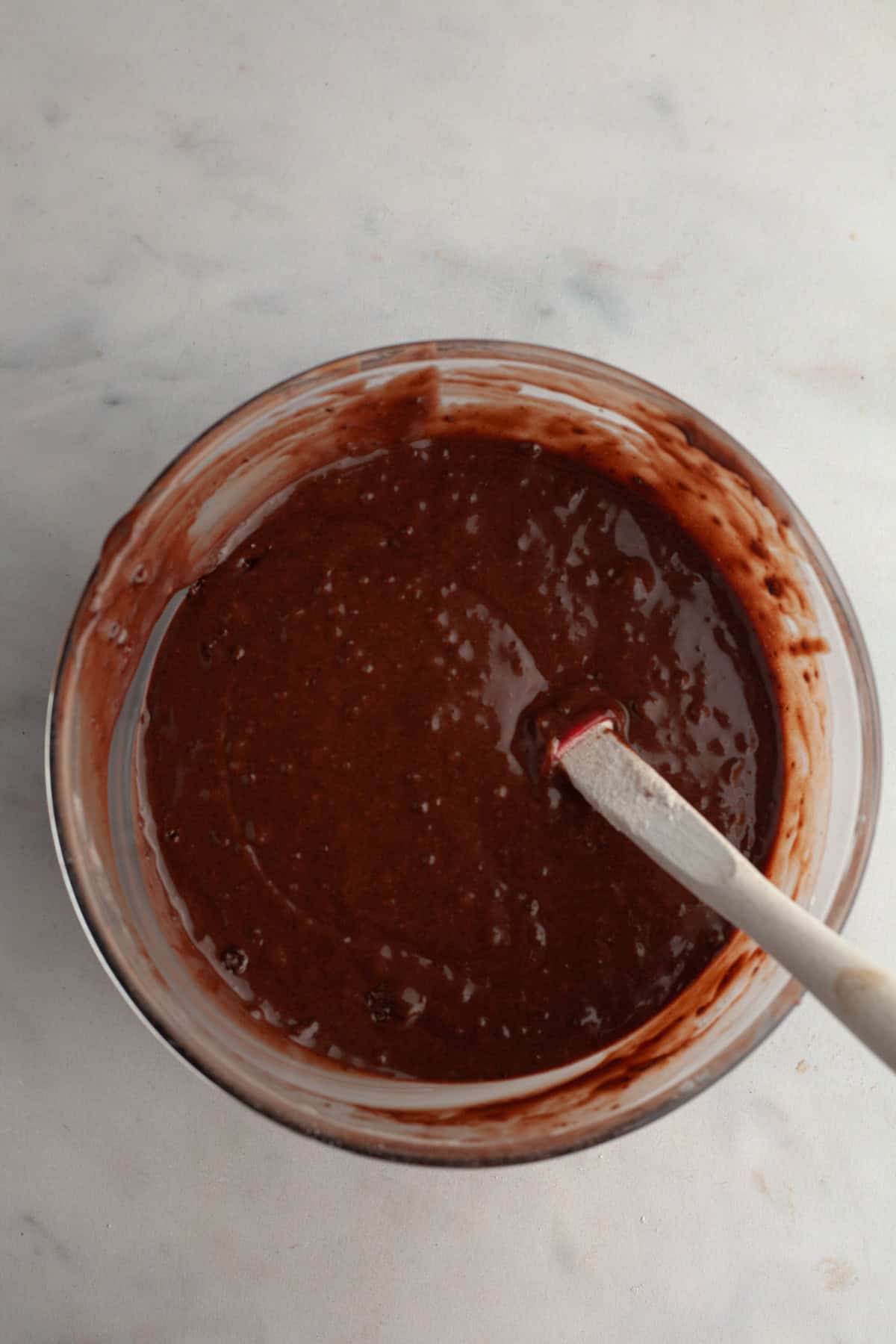 A glass bowl with chocolate muffin batter in it and a rubber spatula.