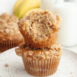 A stack of two banana coffee cake muffins, one has a bite taken out of it.