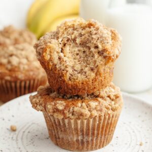 A stack of two banana coffee cake muffins, one has a bite taken out of it.