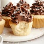 A close up of a coconut cupcake with chocolate frosting with a bite taken out of it.