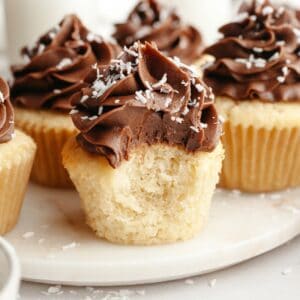 A close up of a coconut cupcake with chocolate frosting with a bite taken out of it.