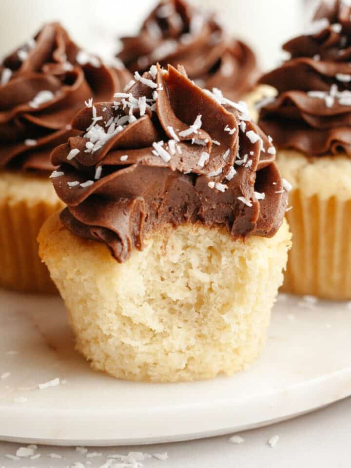 A close up of a coconut cupcake with chocolate frosting with a bite taken out of it.