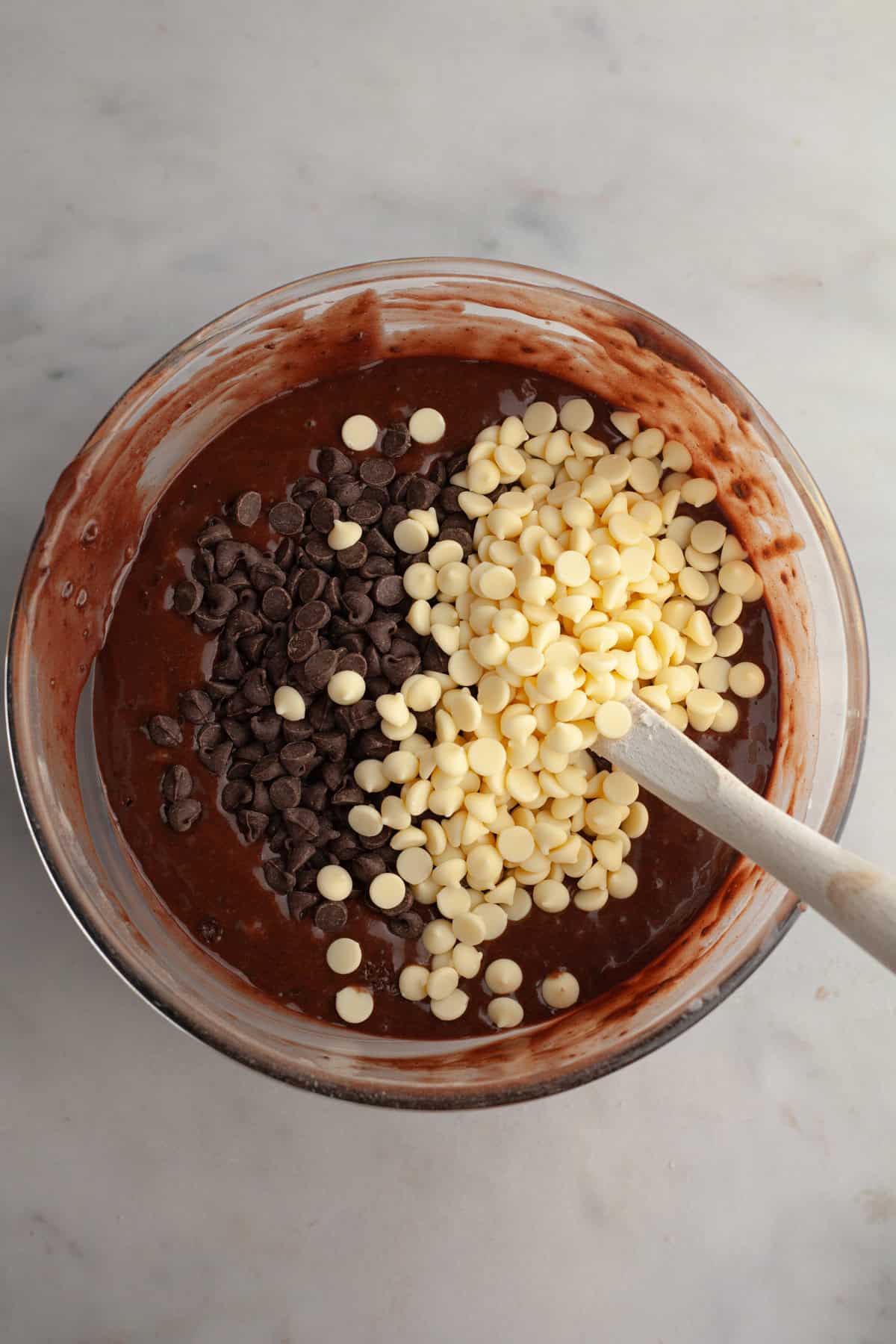 A bowl with chocolate muffin batter and white chocolate chips and chocolate chips.