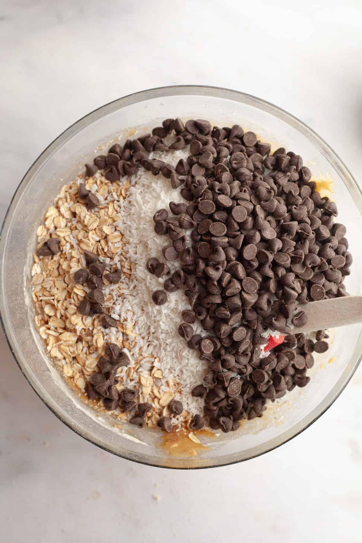 A glass bowl with oats, chocolate chips and shredded coconut.