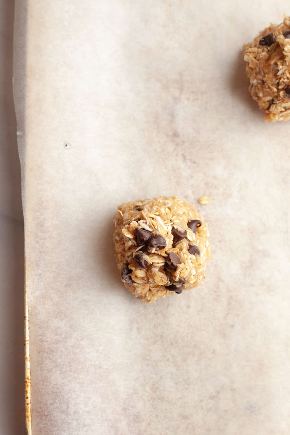 An unbaked oatmeal coconut chocolate chip cookie dough ball on parchment paper.
