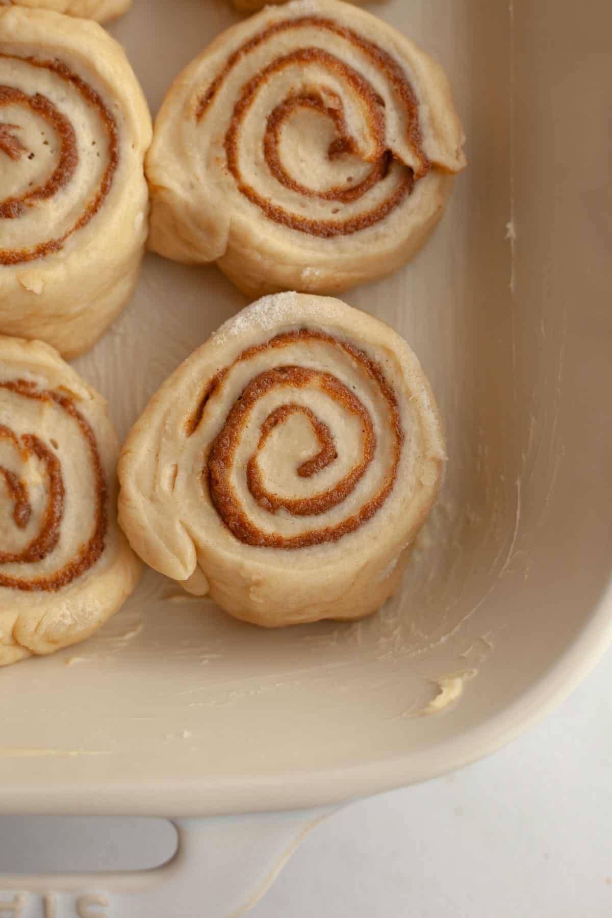 Unbaked cinnamon coffee rolls in a buttered baking dish.