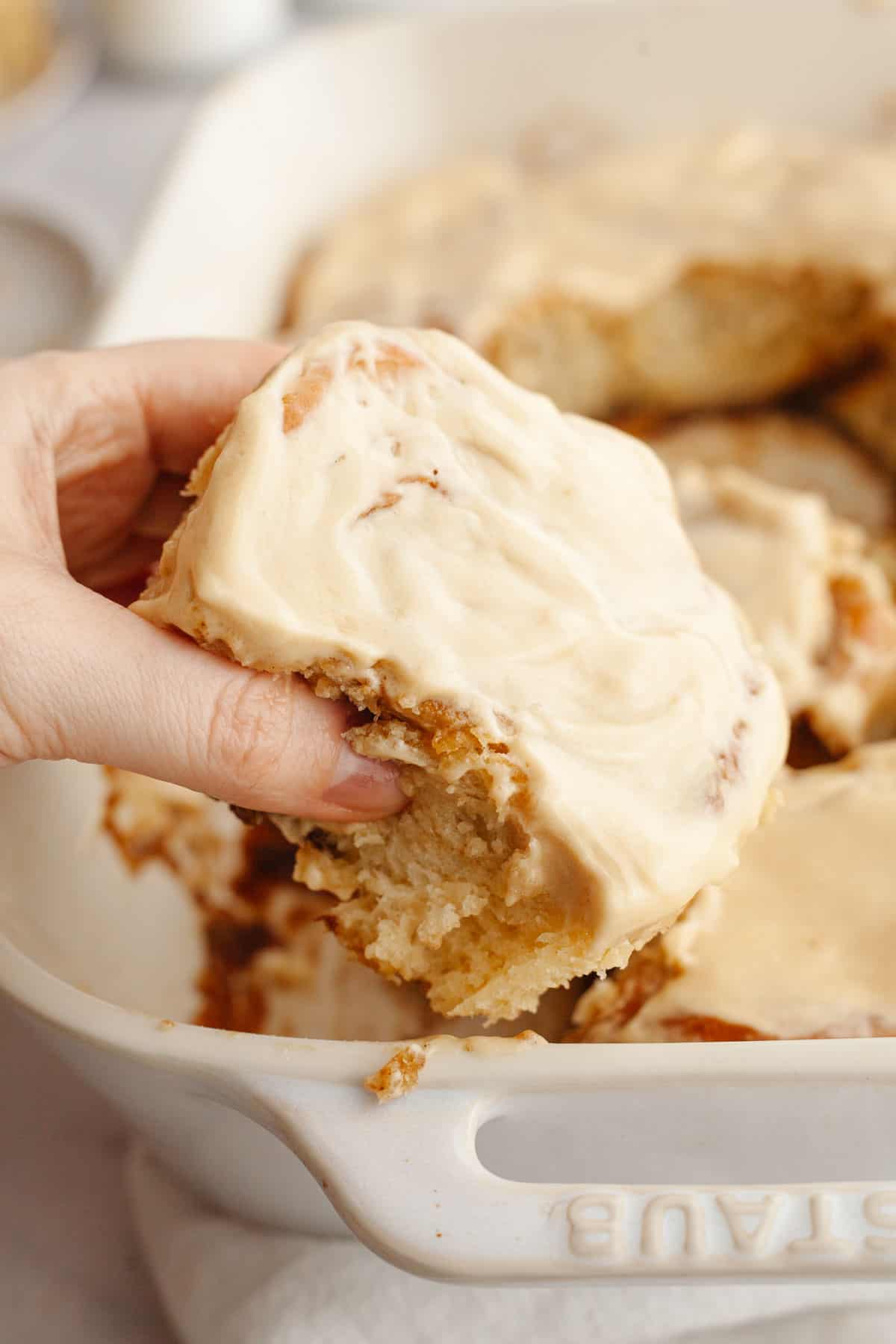 A hand grabbing a cinnamon coffee roll with maple espresso icing.