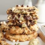 A stack of pistachio chocolate chip cookies broken in half, showing that the inside is filled with pistachio cream.
