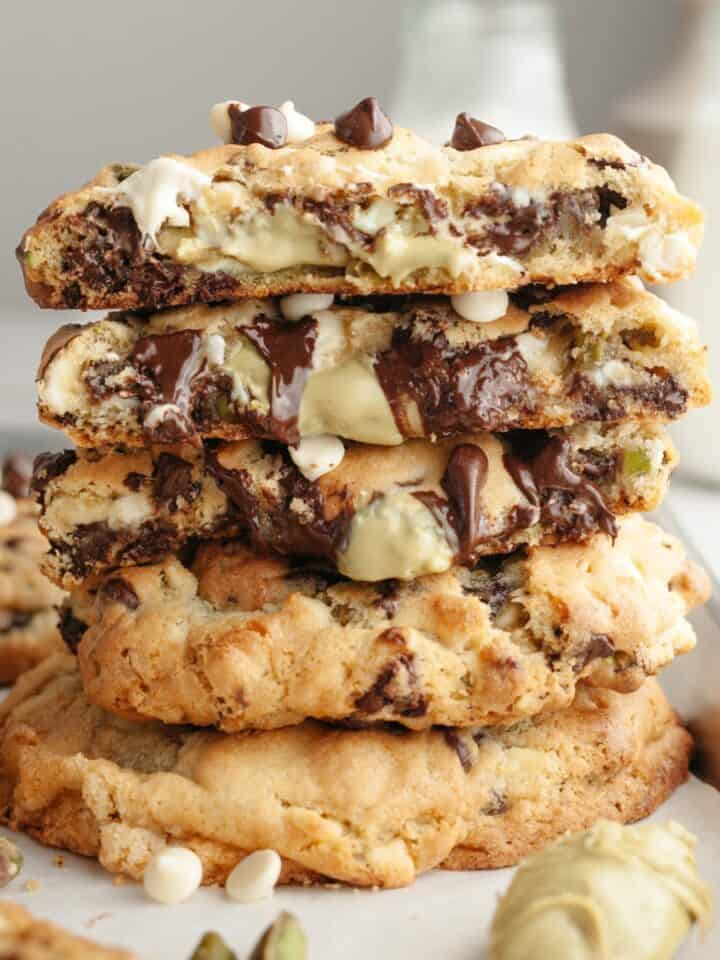 A stack of pistachio chocolate chip cookies broken in half, showing that the inside is filled with pistachio cream.