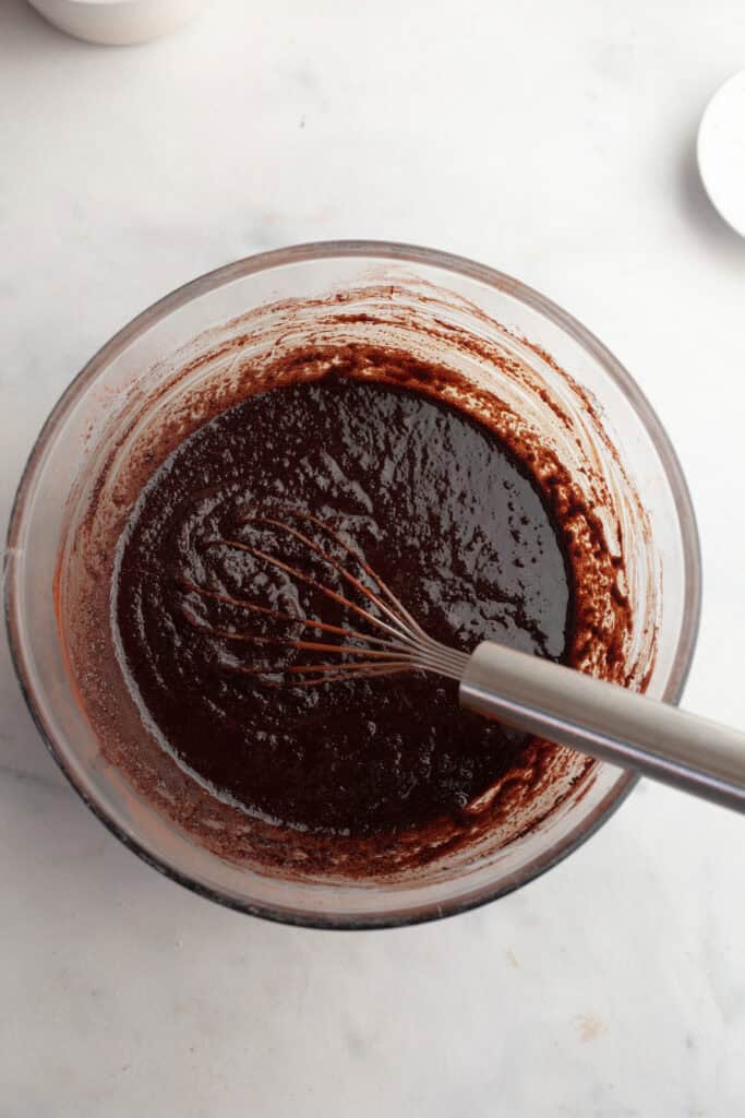 A glass bowl with brownie batter and a whisk.