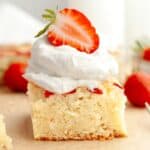 A close up of a slice of a mini strawberry cake, topped with whipped cream and half of a fresh strawberry.