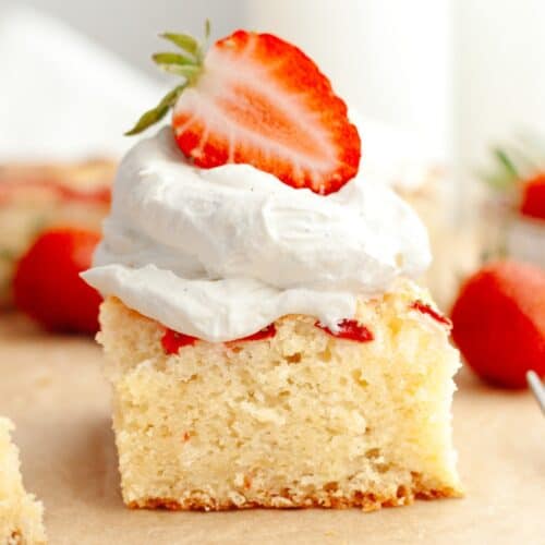 A close up of a slice of a mini strawberry cake, topped with whipped cream and half of a fresh strawberry.