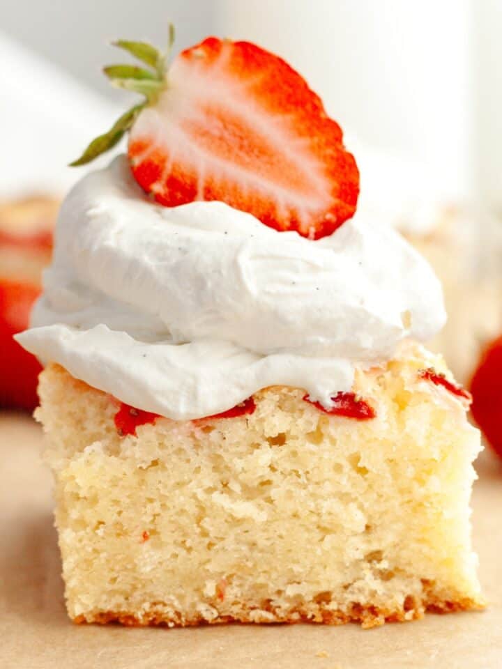 A close up of a slice of a mini strawberry cake, topped with whipped cream and half of a fresh strawberry.