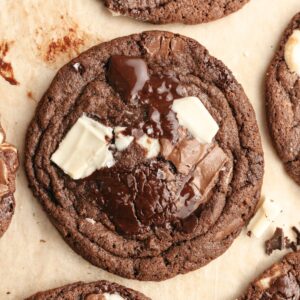 A close up of a triple chocolate chunk cookie on brown parchment paper.