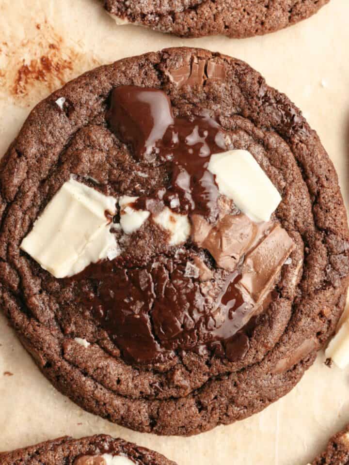 A close up of a triple chocolate chunk cookie on brown parchment paper.