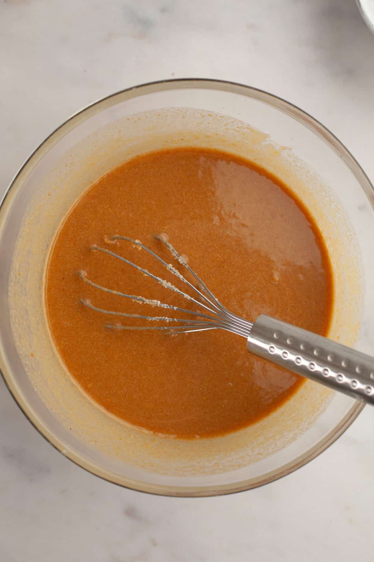 A light brown liquid in a glass bowl with a whisk.