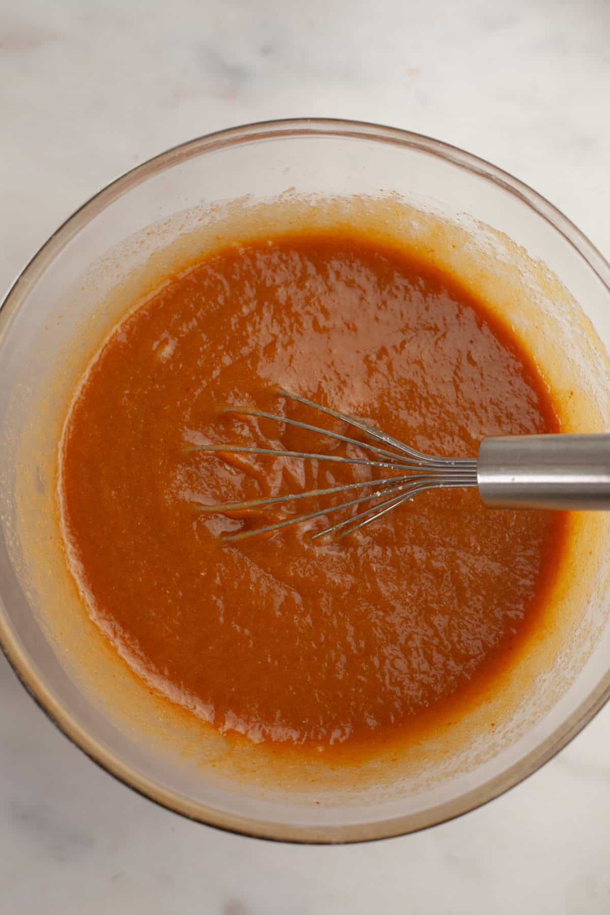 Light brown liquid in a glass bowl with a whisk.