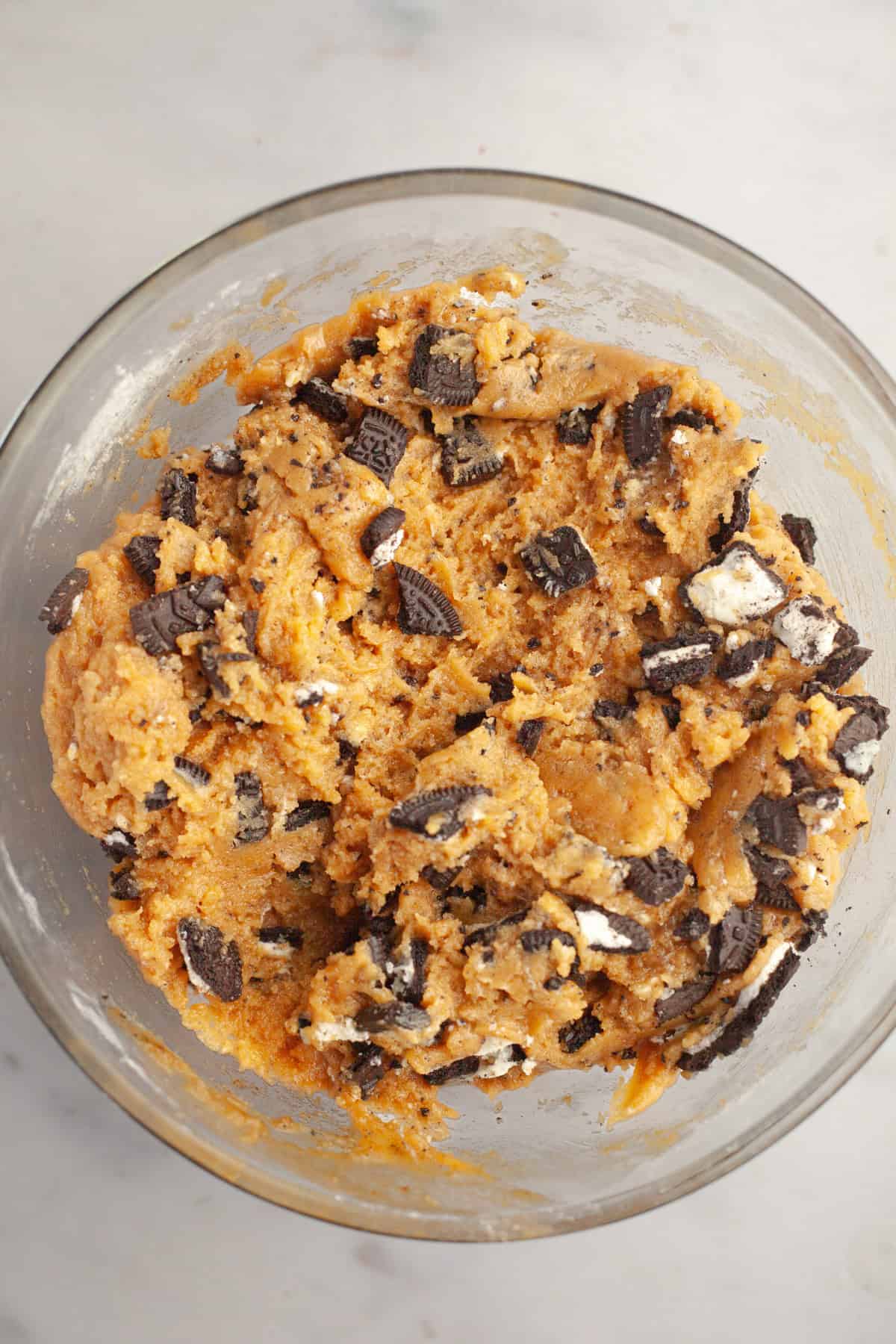 Peanut butter cookie dough with chopped Oreos in a glass bowl.