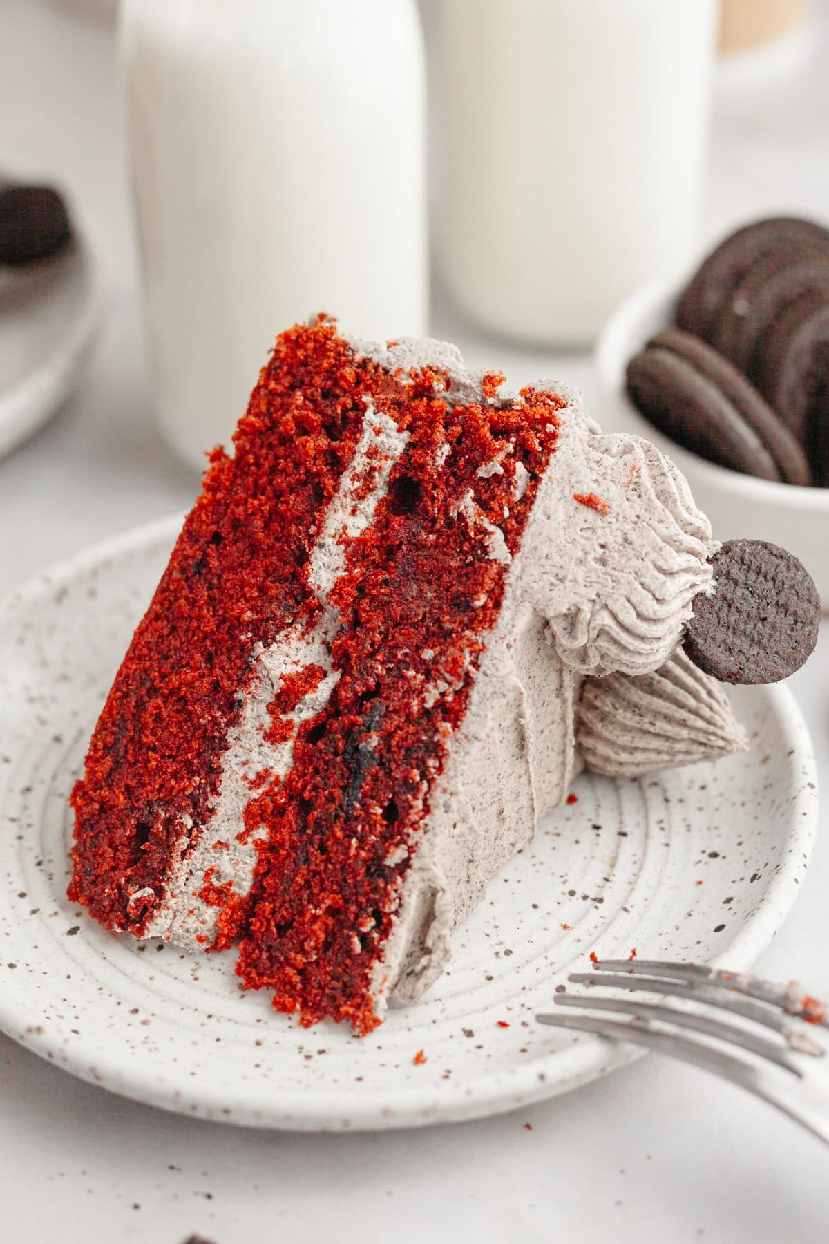 A slice of red velvet cake with Oreo frosting on a small plate.