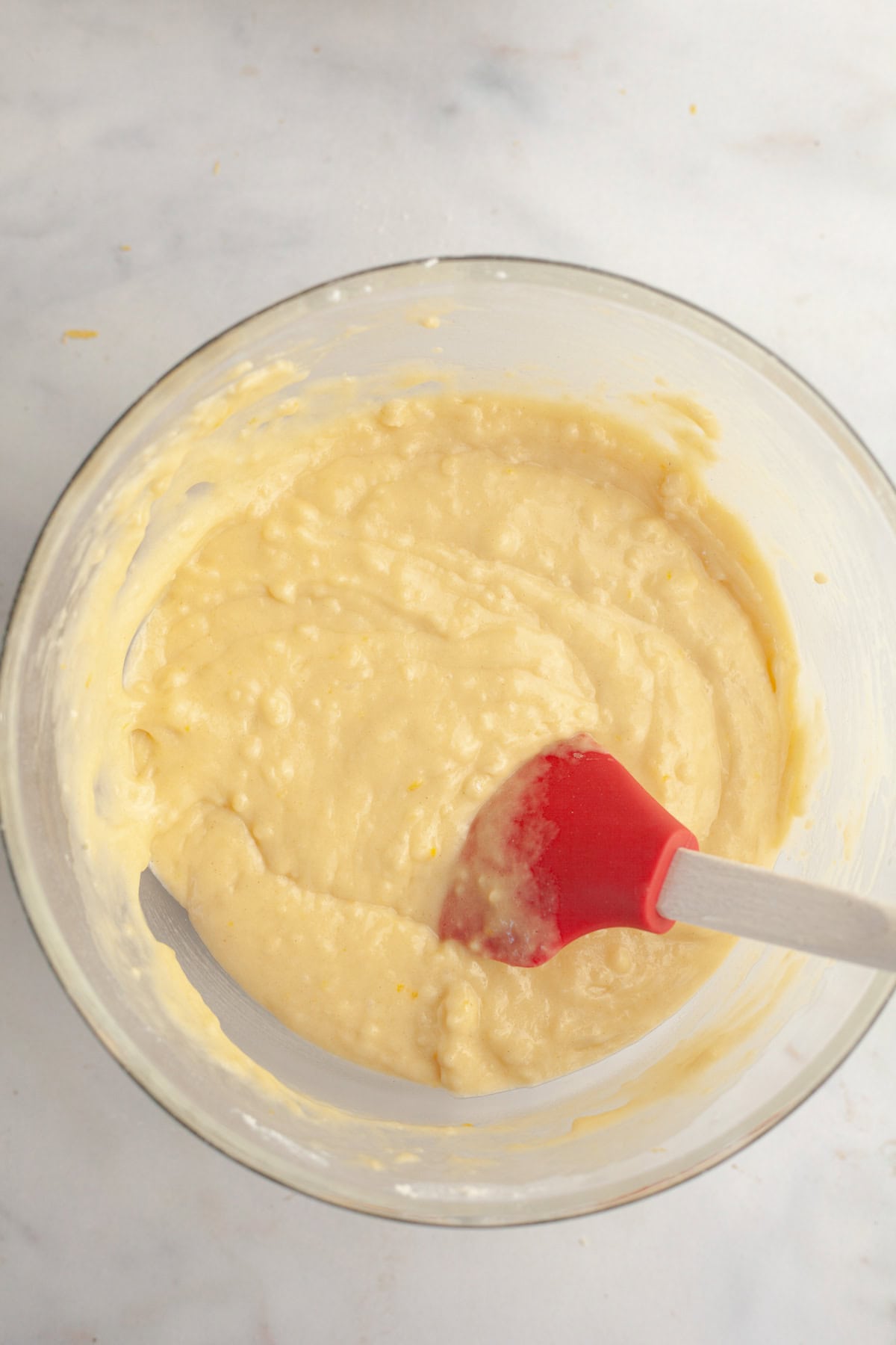 Vanilla cake batter in a glass bowl with a rubber spatula.