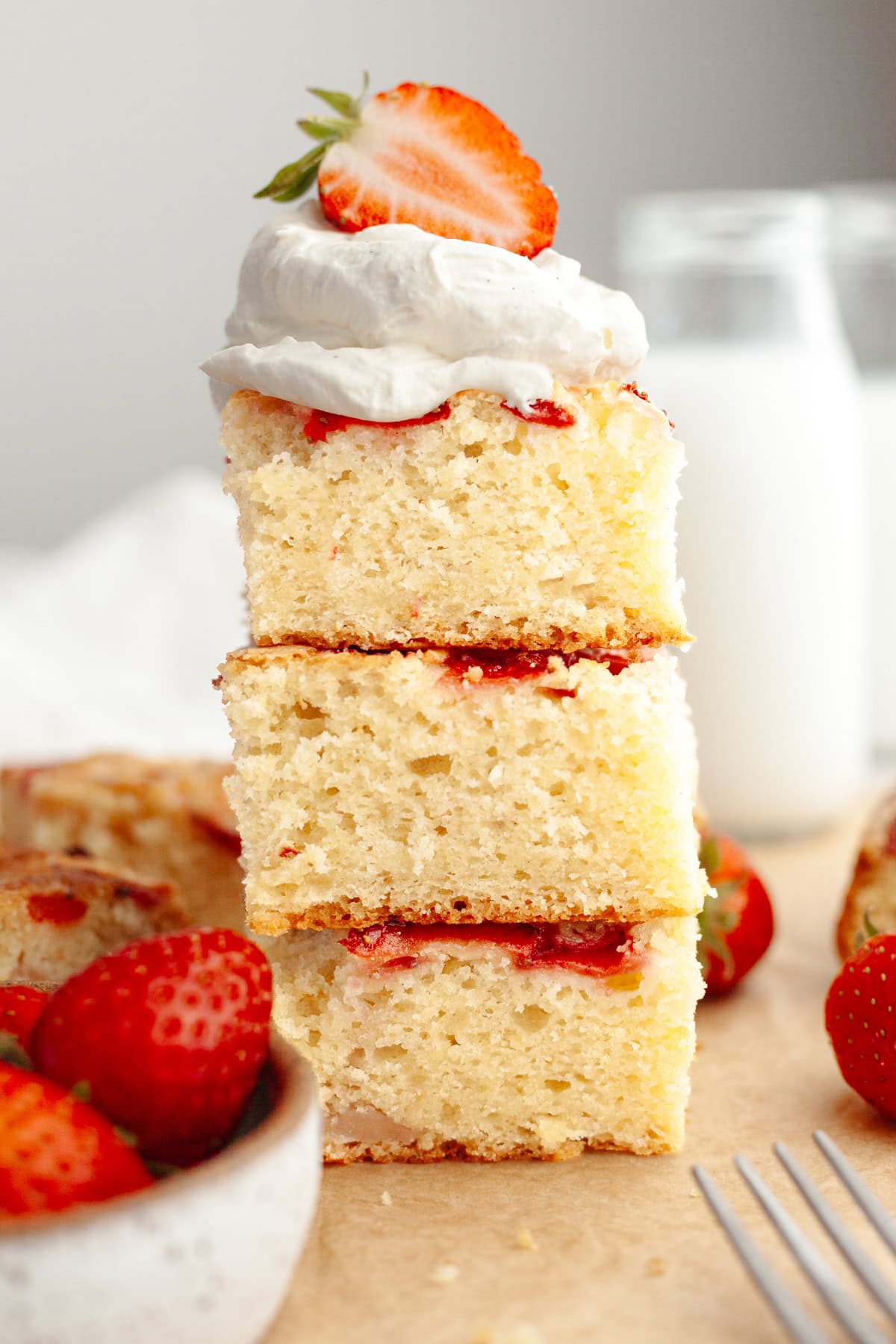 Three slices of mini strawberry cake stacked on top of each other, topped with whipped cream and a strawberry.