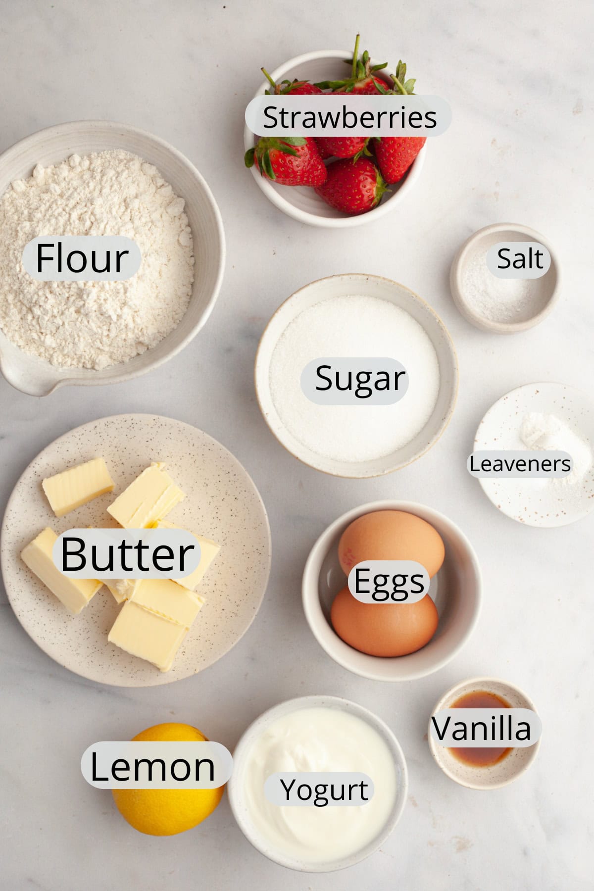 All the ingredients needed to make a mini strawberry snack cake, weighed out into small bowls.
