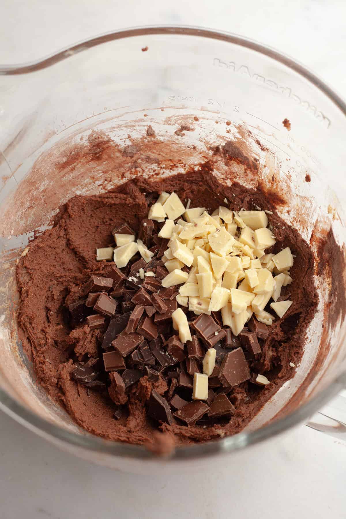 Chocolate cookie dough in a glass bowl with chopped chocolate.