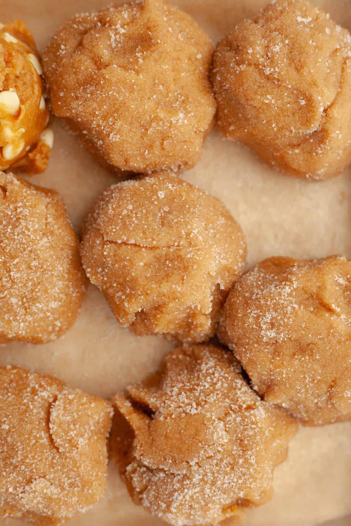 Peanut butter cookie dough balls rolled in white sugar on parchment paper.