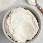 A light grey bowl filled with mascarpone whipped cream frosting.