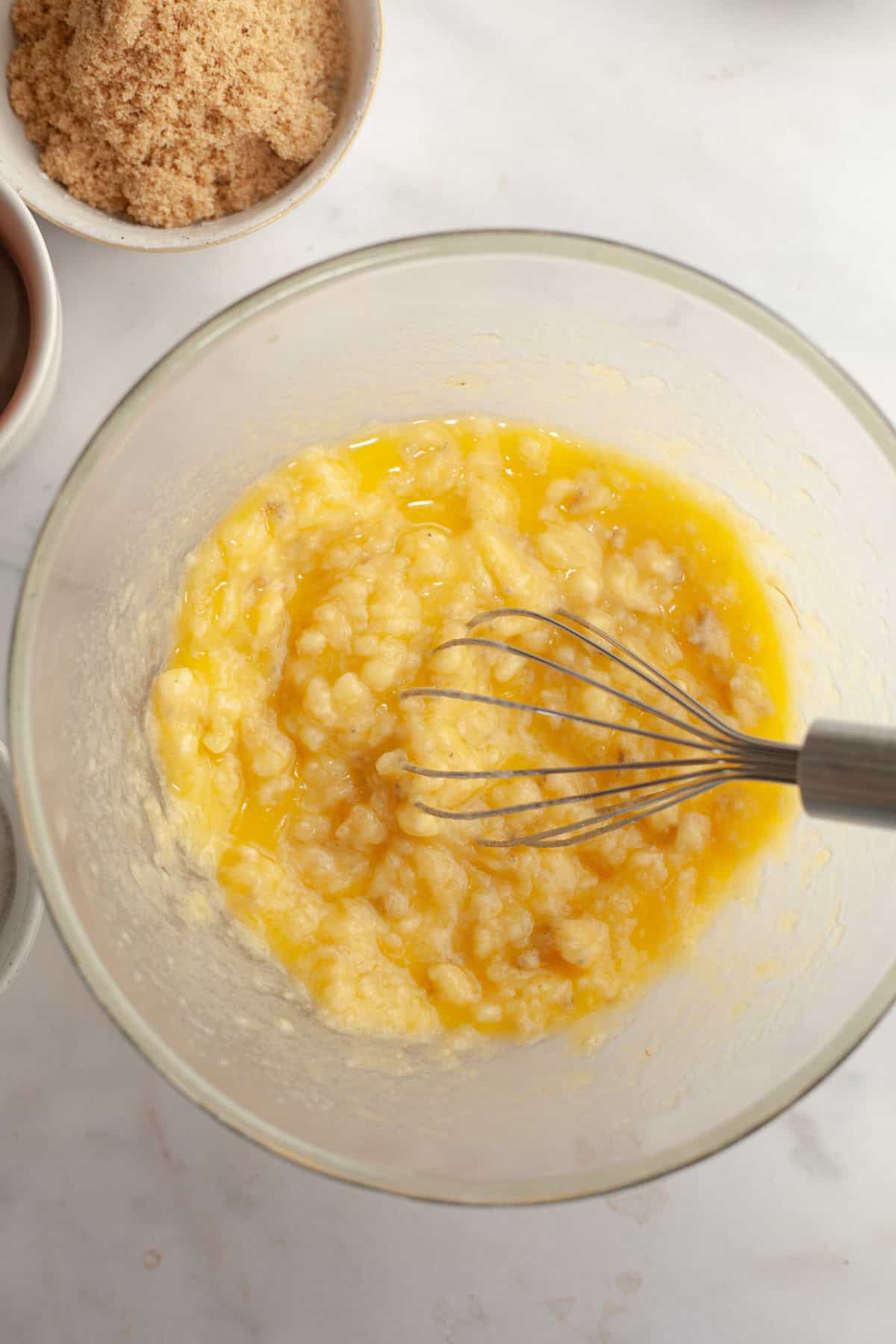 A large glass bowl with butter and mashed banana in it.