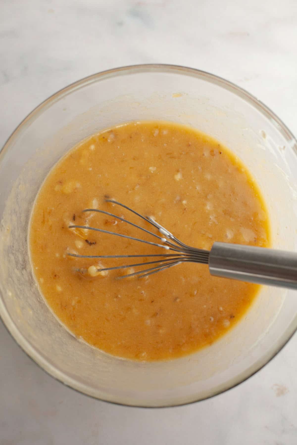 A large glass bowl with a whisk and banana bread batter.
