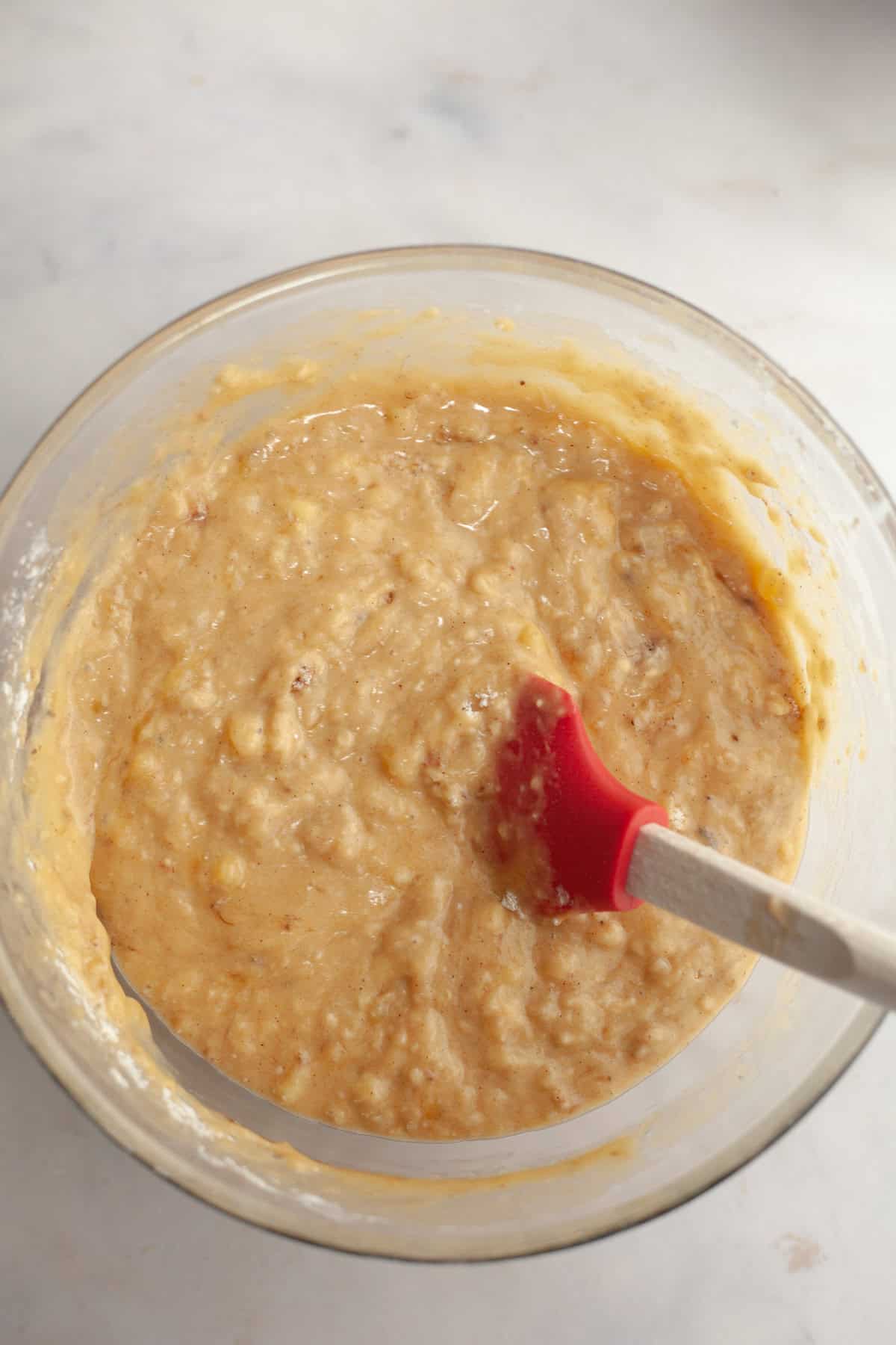 A large glass bowl with a rubber spatula and banana bread batter.