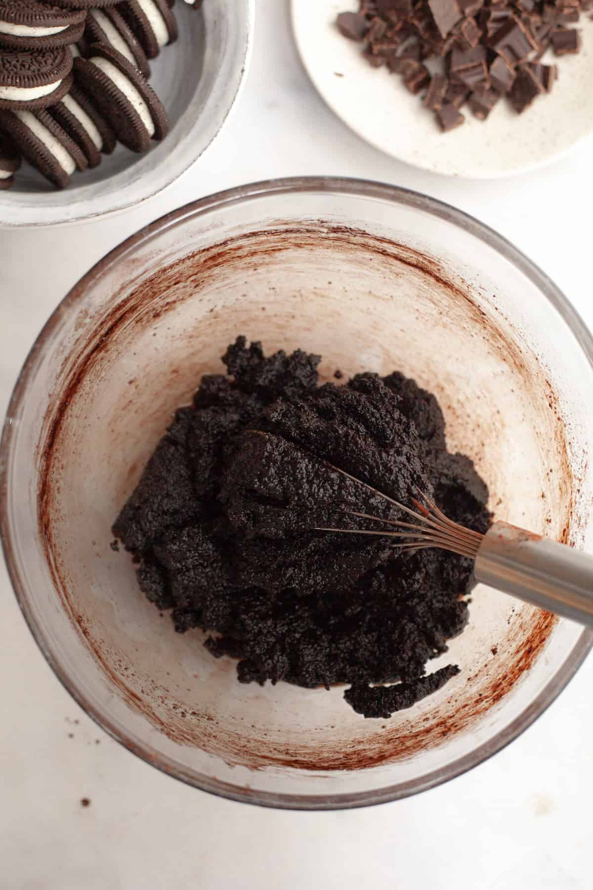 A glass bowl with a whisk and brownie batter.