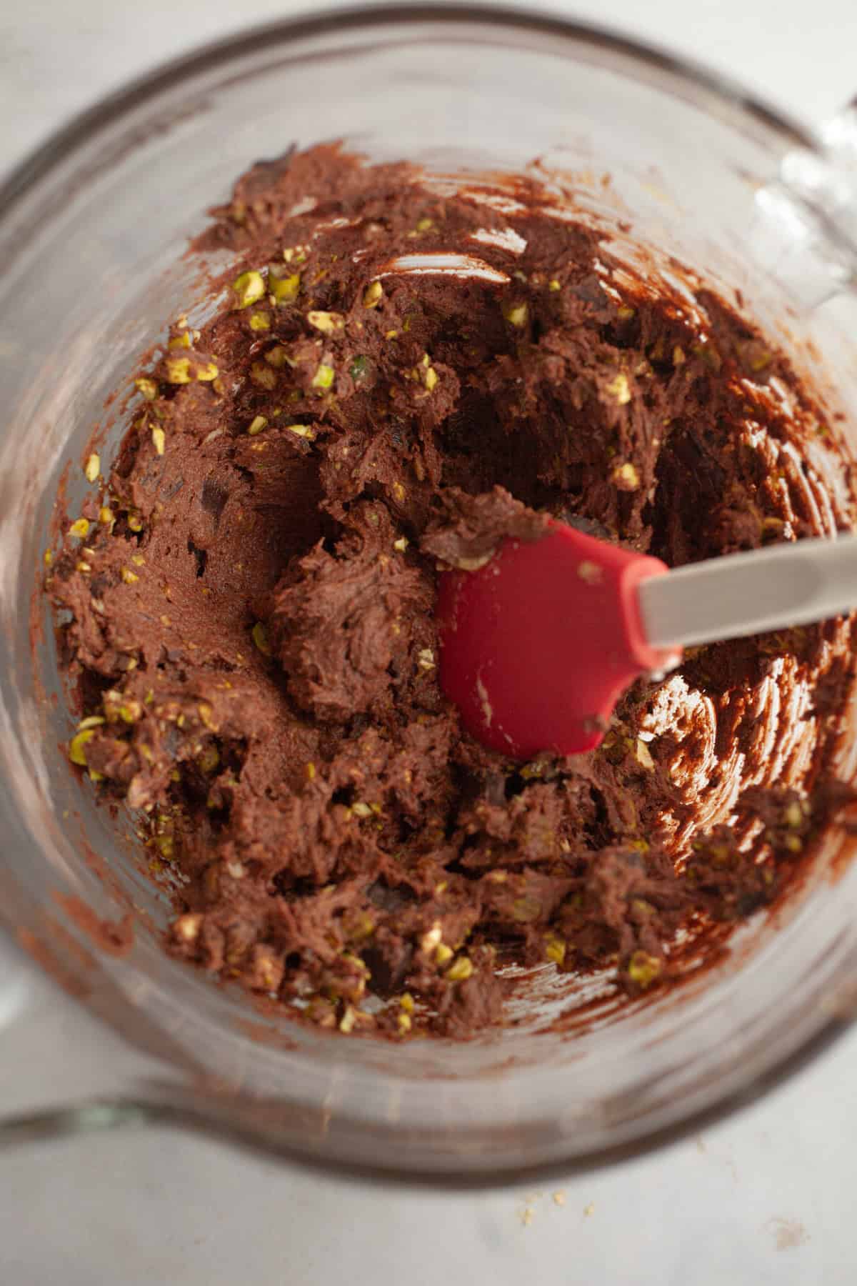 Chocolate cookie dough with chopped pistachios in a glass bowl.