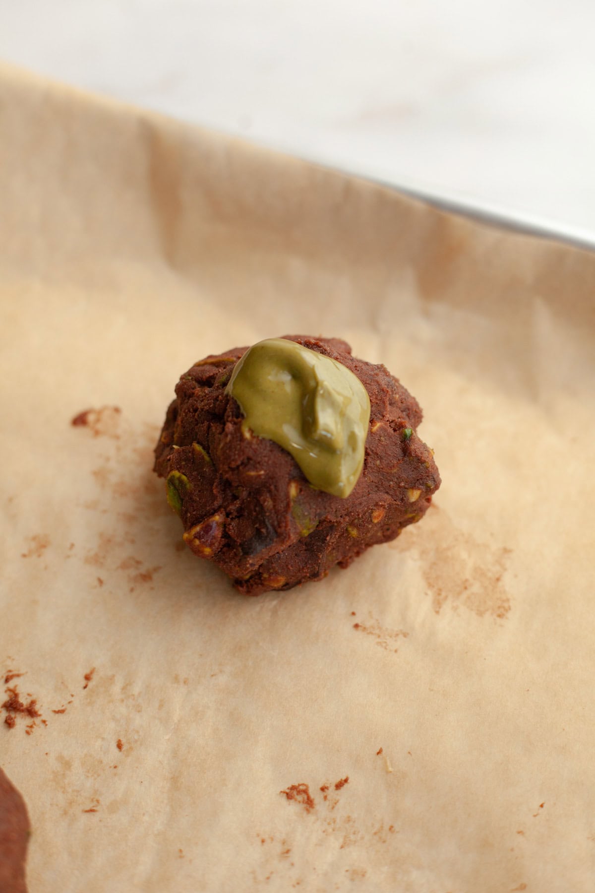 An unbaked chocolate cookie dough ball topped with pistachio cream.