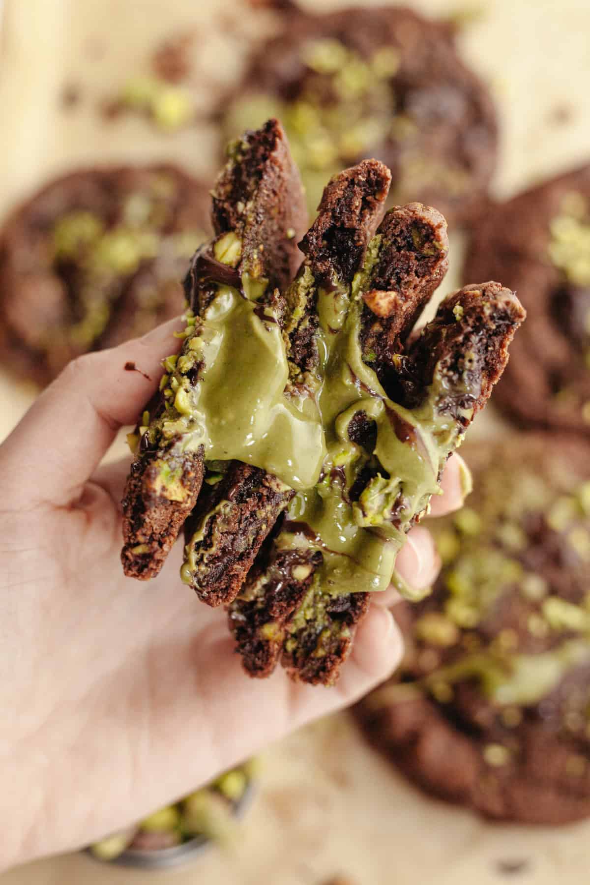 A hand holding chocolate cookies cut in half, showing a pistachio cream center.