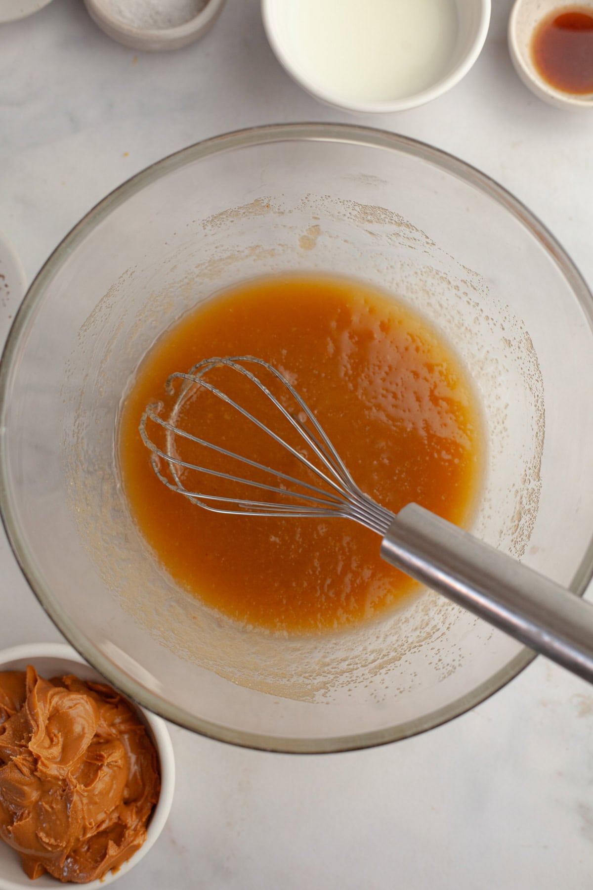 A glass bowl with a light brown mixture in it and a whisk.