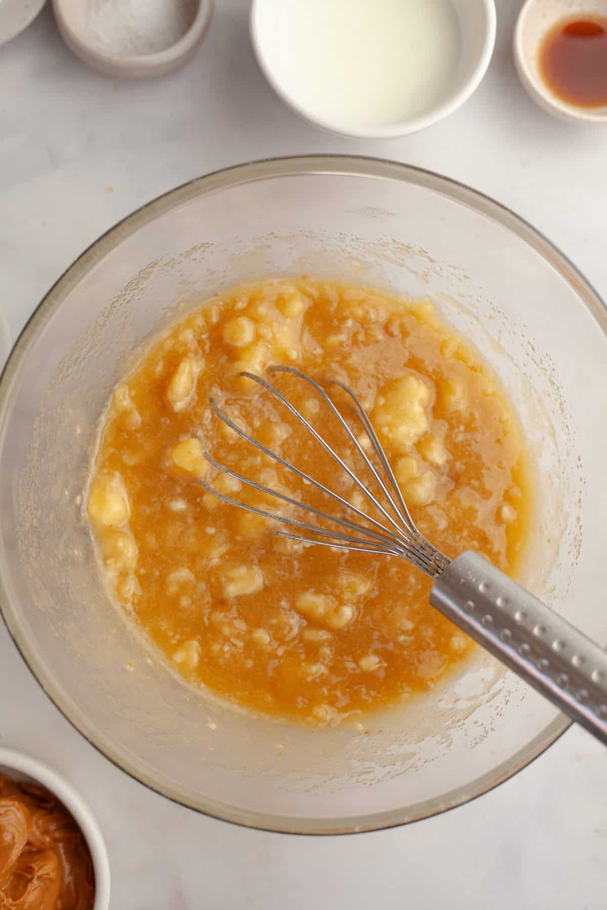 Banana cake mixture in a glass bowl with a whisk.