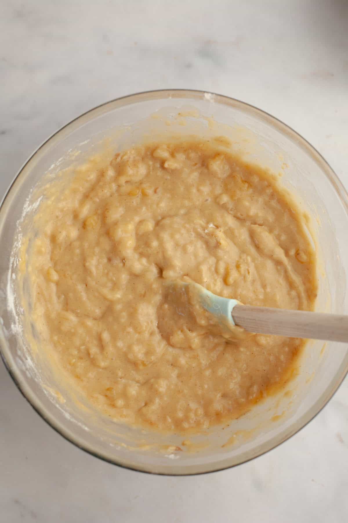 Banana cake mixture in a glass bowl with a rubber spatula.