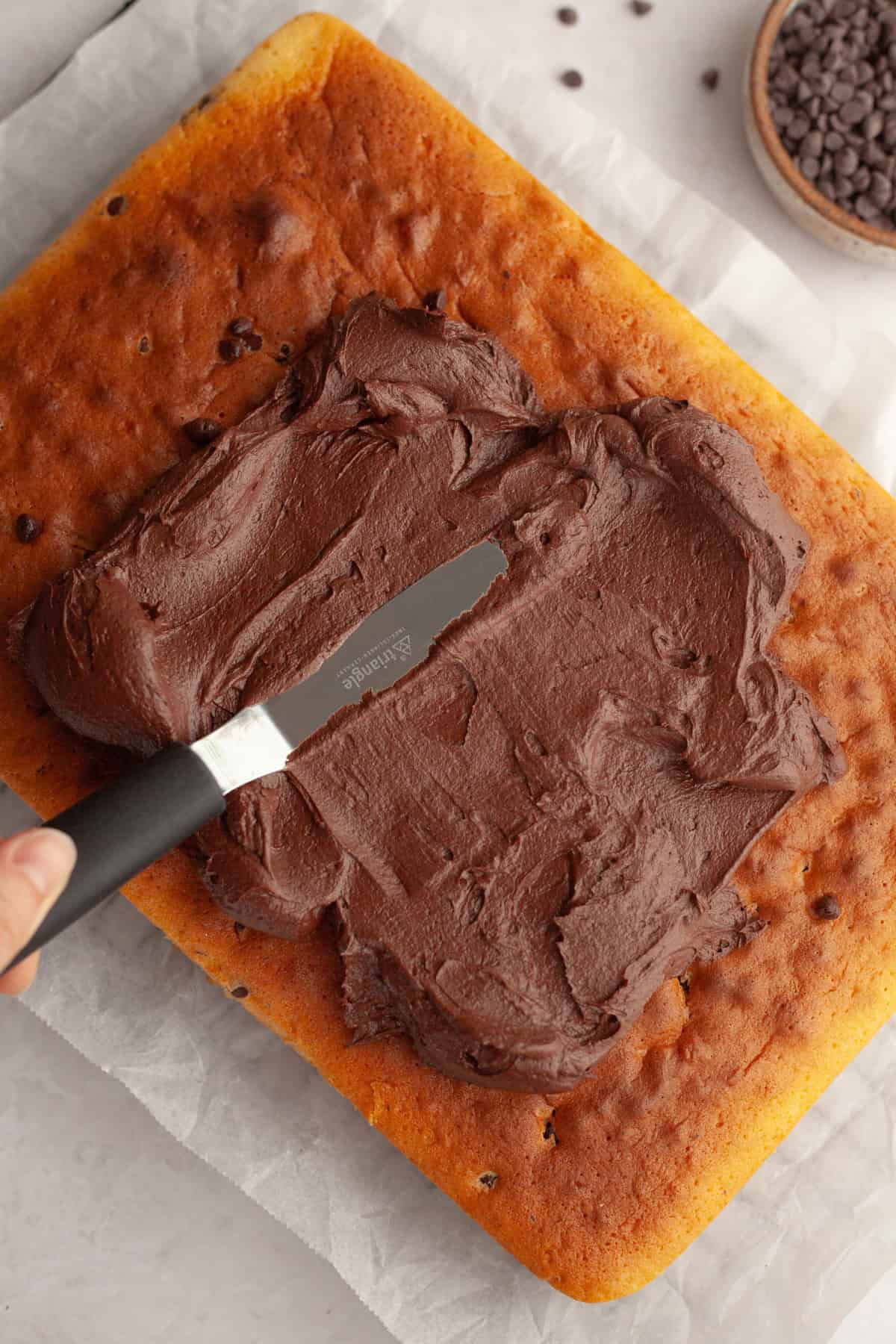 Chocolate frosting being spread onto a rectangular sheet cake.