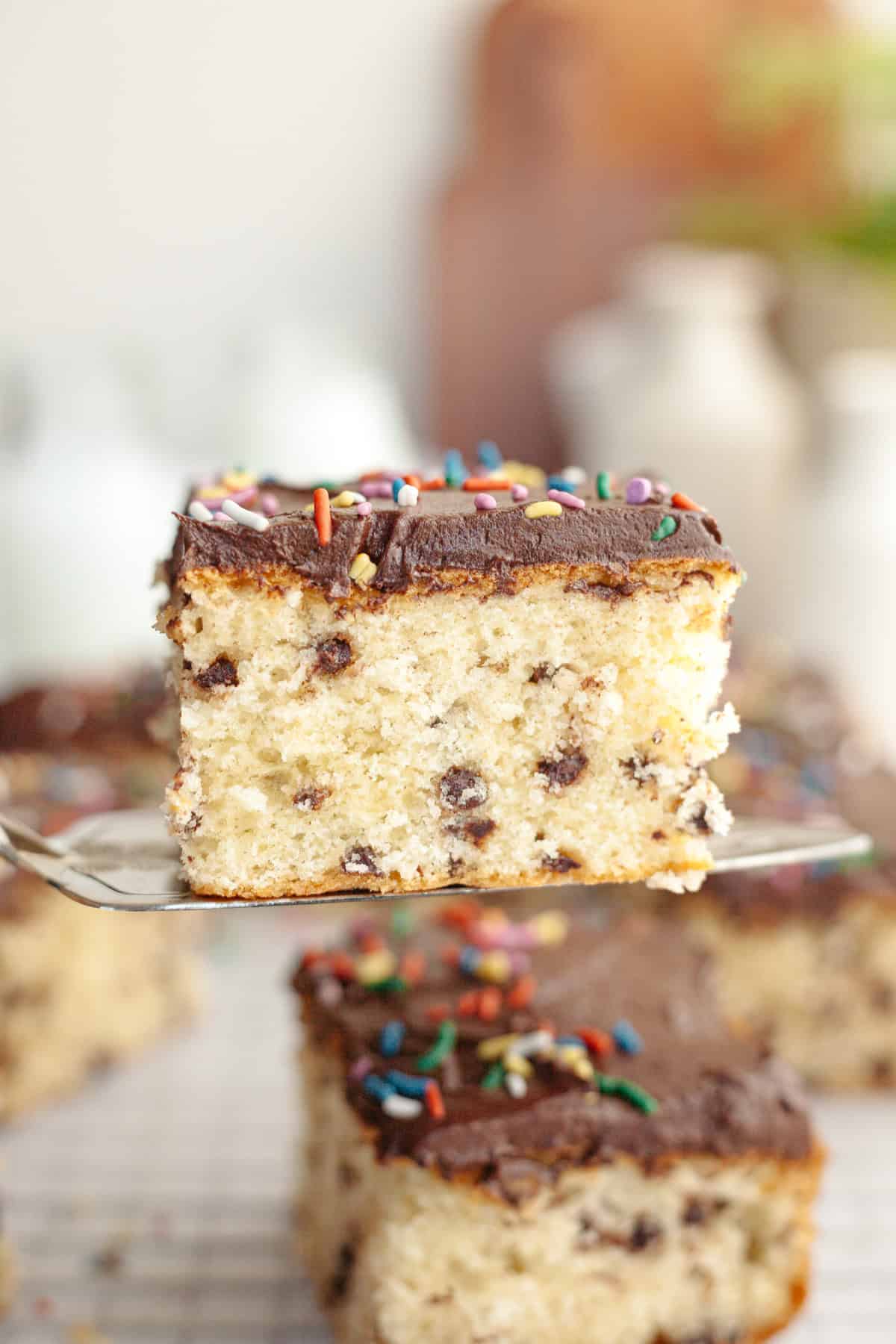 A close up of a slice of chocolate chip sheet cake with chocolate frosting on a cake server.