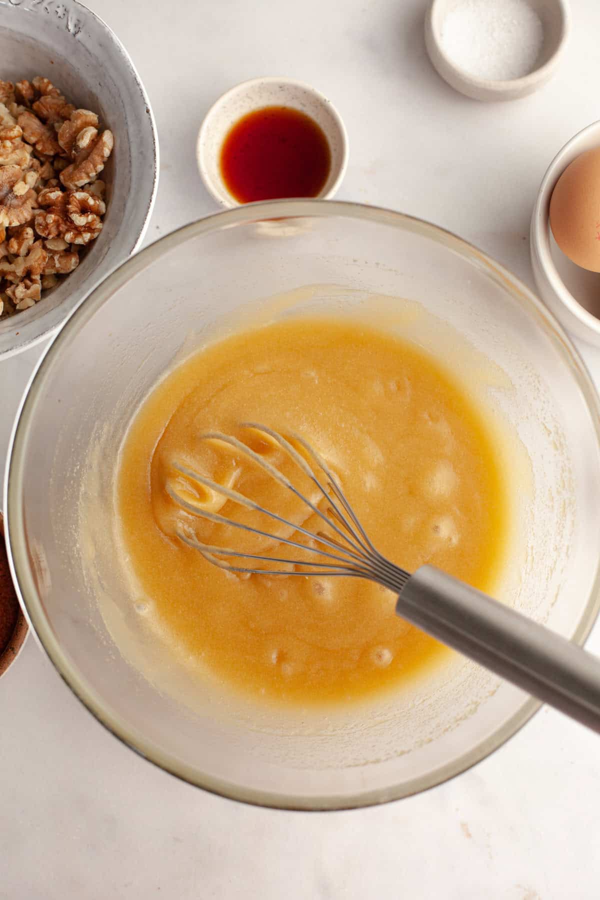 A glass bowl with a whisk and a yellow mixture in it.
